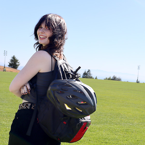 Photo of a younf woman in a field of grass looking over her shoulder with a bike helmet clipped onto her backpack